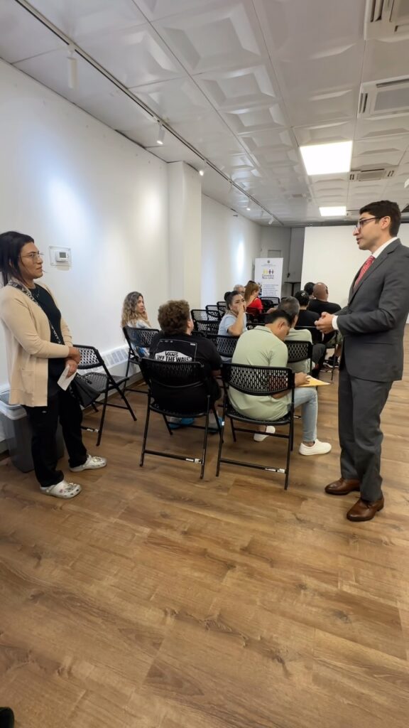 Personas sentadas en una sala del Consulado de Colombia en Nueva York mientras un funcionario conversa con una asistente, imagen del video sobre las nuevas medidas sin cita